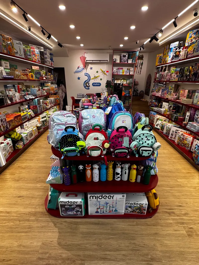 The main aisle of the Toy Gate shop in Saida: a red display island of backpacks, water bottles and Mideer boxes between two walls of toy shelves.