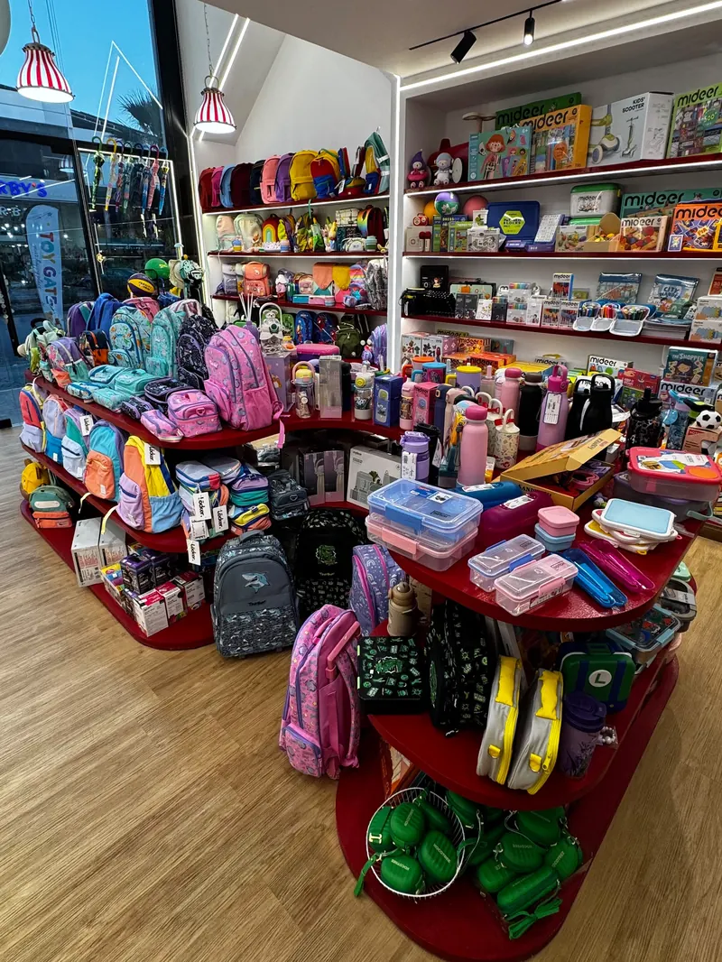 Round red display islands stacked with school bags, lunch boxes and bottles, with wall shelves of toys behind.